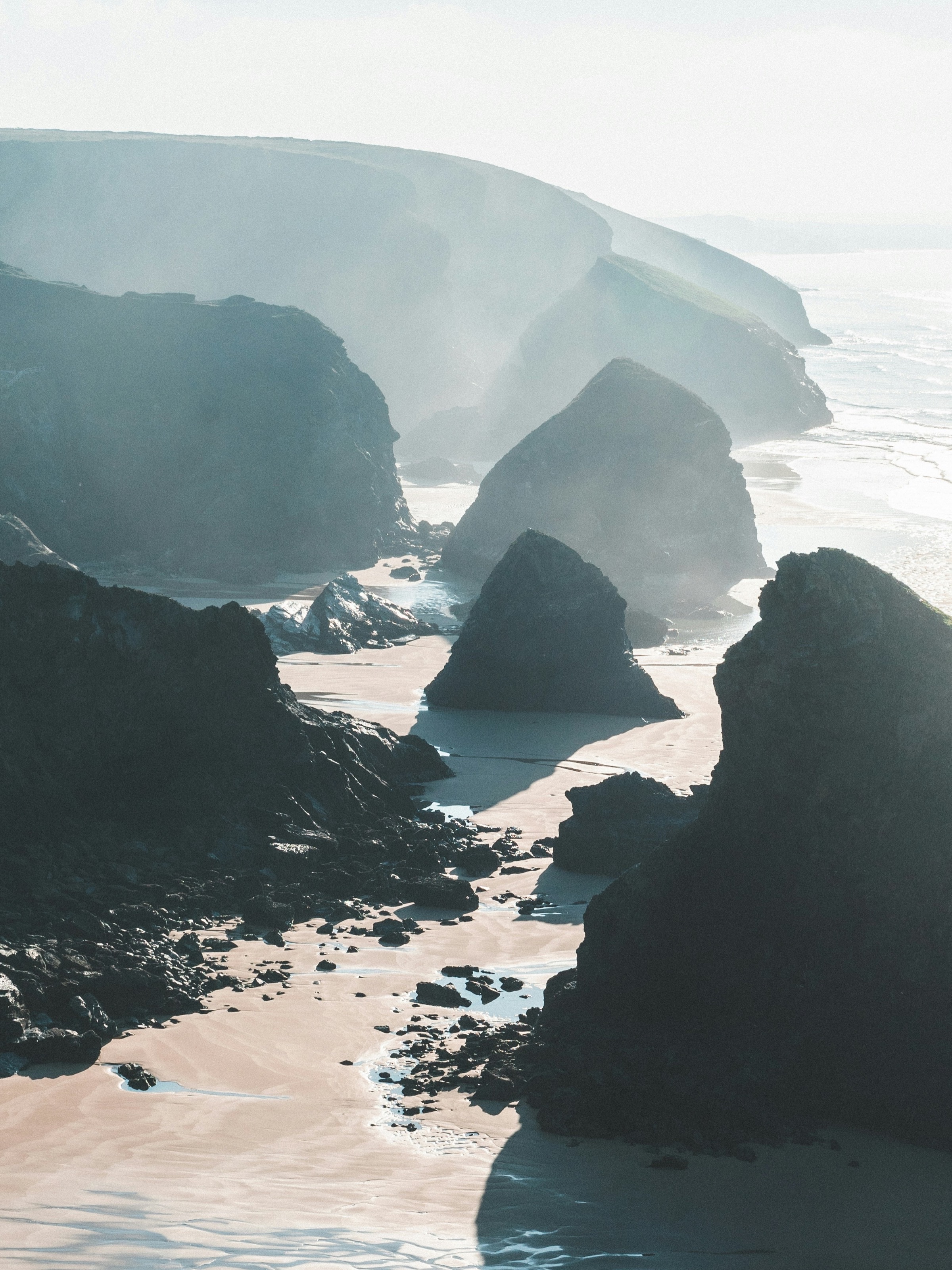 The rock stacks of Bedruthan Steps seen from the clifftop in hazy light, the tide far out
