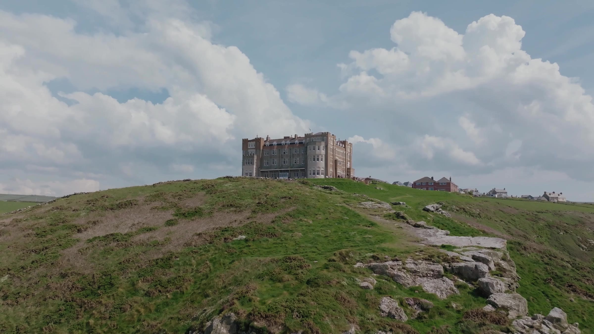 A castellated hotel on a grassy clifftop headland, with a village beyond