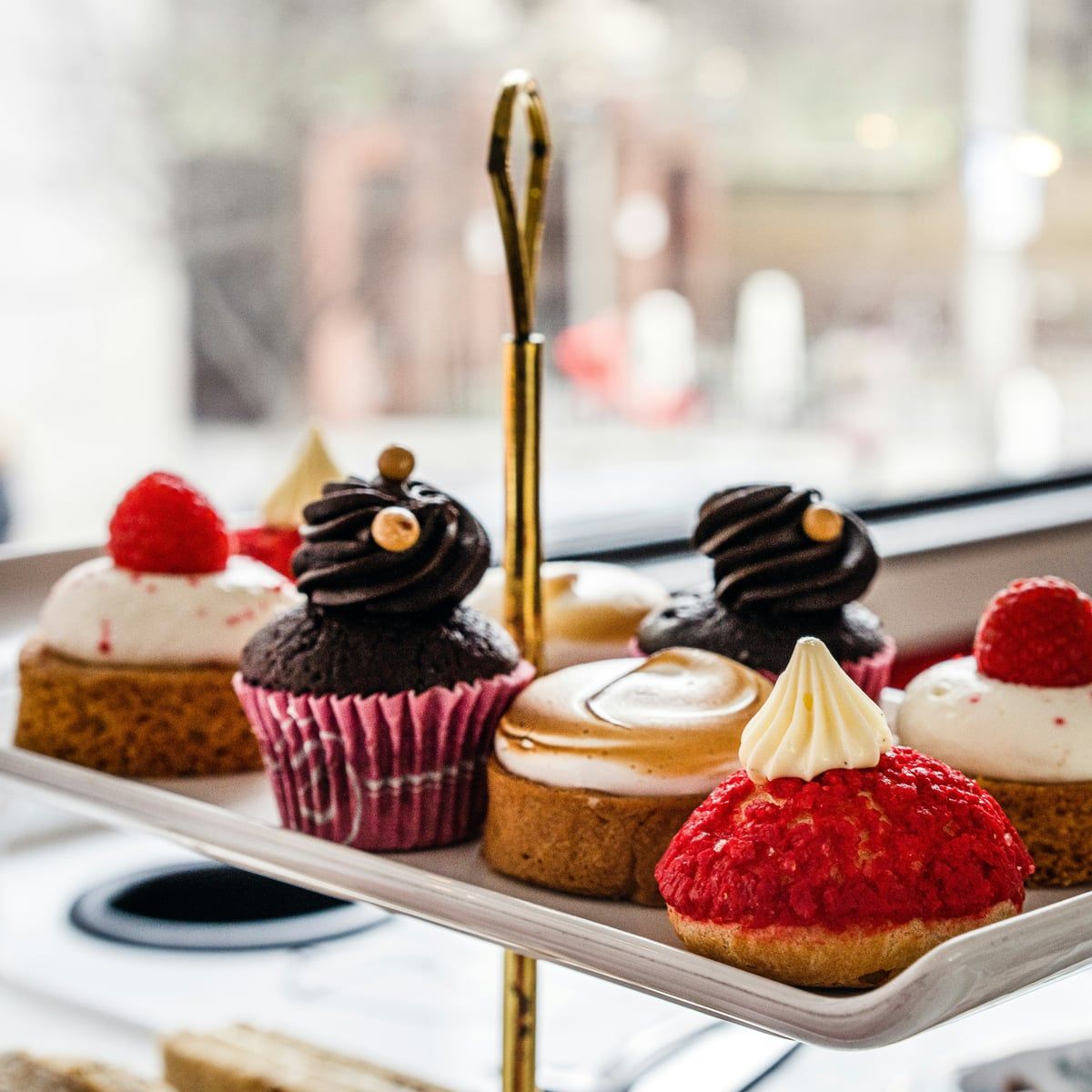 A tiered stand of afternoon tea cakes and pastries beside a window