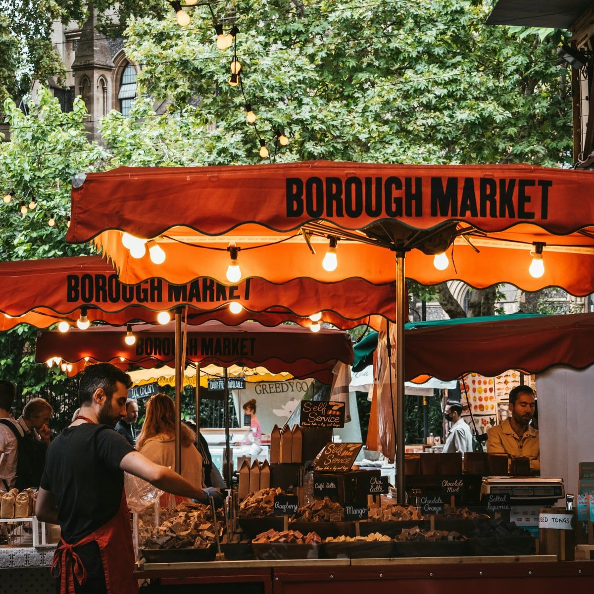 A busy food stall under the Borough Market awning, lit with strings of bulbs
