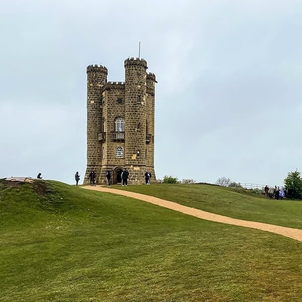 Broadway Tower on its grassy Cotswolds ridge, walkers on the path leading up to it
