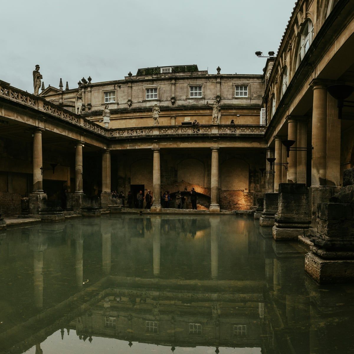 The Great Bath at the Roman Baths at dusk, lamps glowing along the colonnade