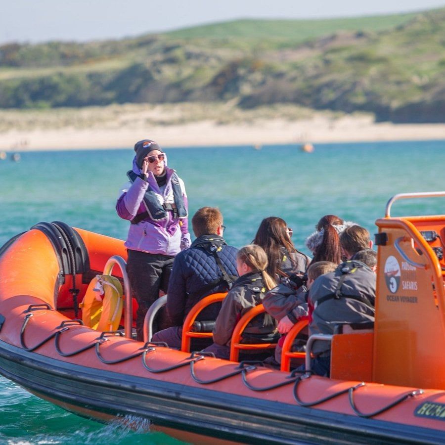 Passengers in an orange rigid inflatable boat on turquoise water, a sandy shore behind