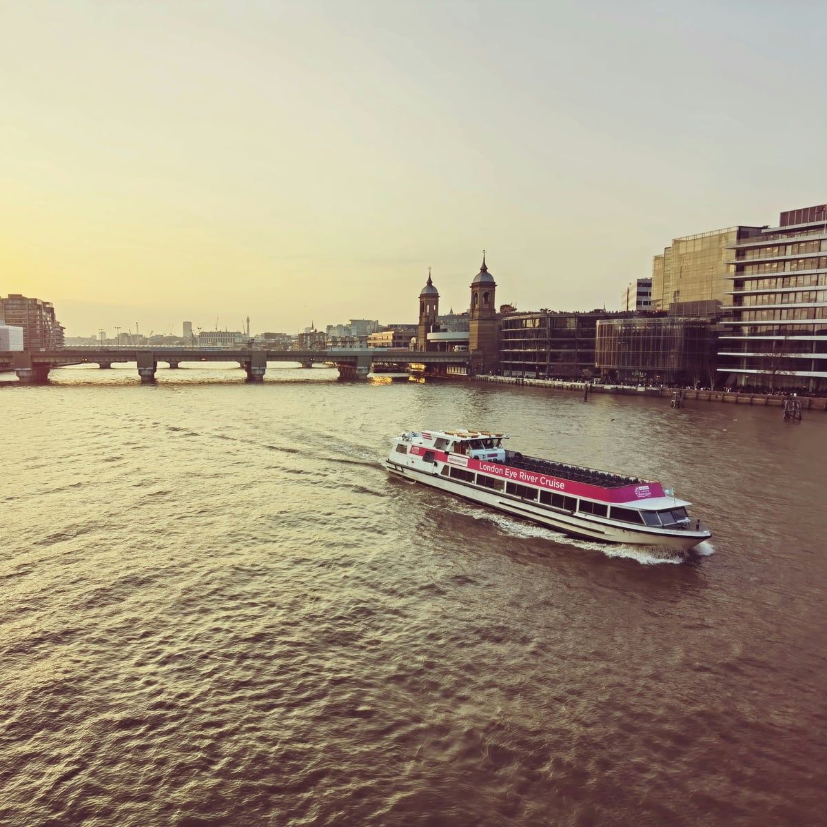A river cruiser on the Thames at sunset, a bridge and the City skyline beyond