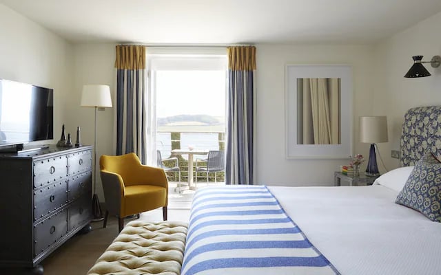 A bedroom at Hotel Tresanton, a striped throw on the bed and French windows opening to a balcony over the water