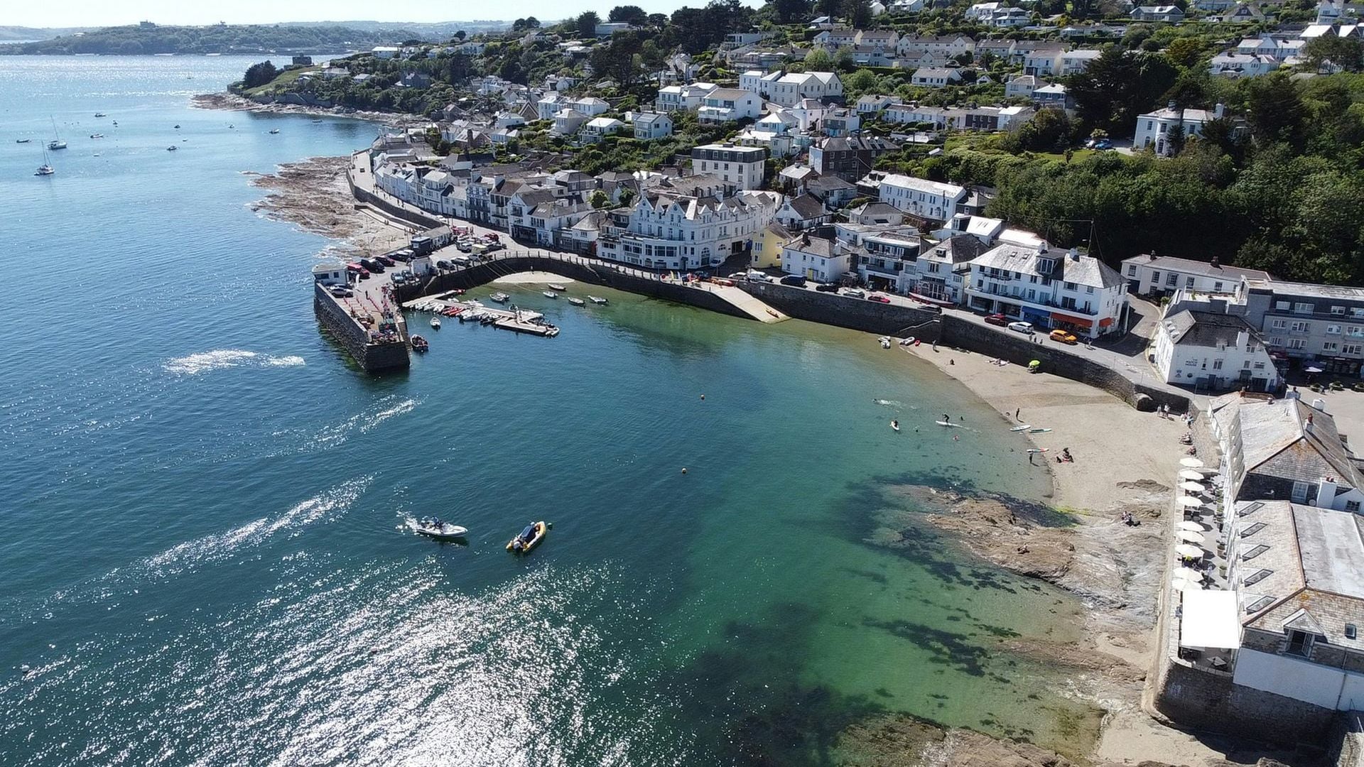 St Mawes from the air, white houses climbing the hill above the harbour wall and the clear green water of the bay