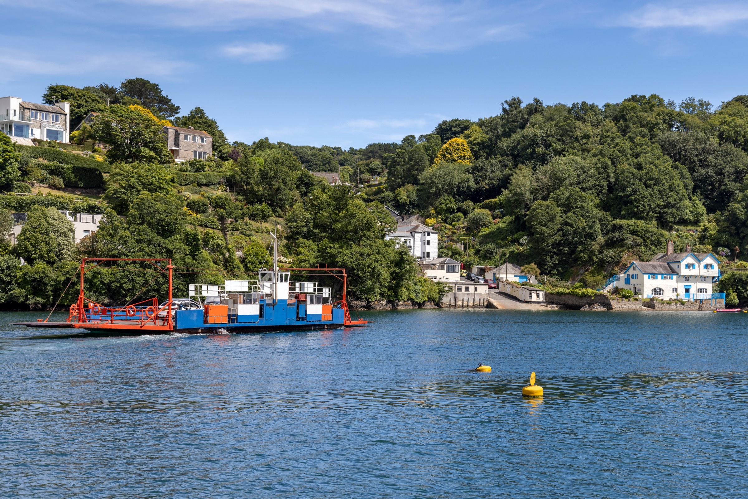 A chain ferry crossing a wooded river estuary lined with houses